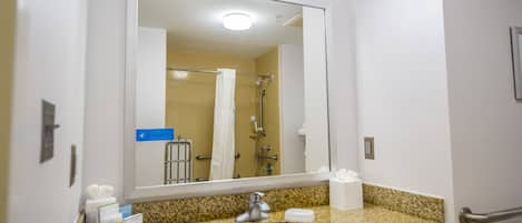 Une salle de bain avec un comptoir en granit, un lavabo, un miroir, un porte-serviettes et une douche dont on aperçoit le reflet.