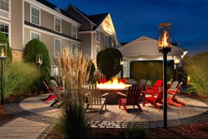 A patio with a fire pit, outdoor seating, and a well-lit building in the background.