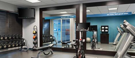 Un gimnasio con equipo de ejercicio, un televisor y un letrero motivacional en la pared.