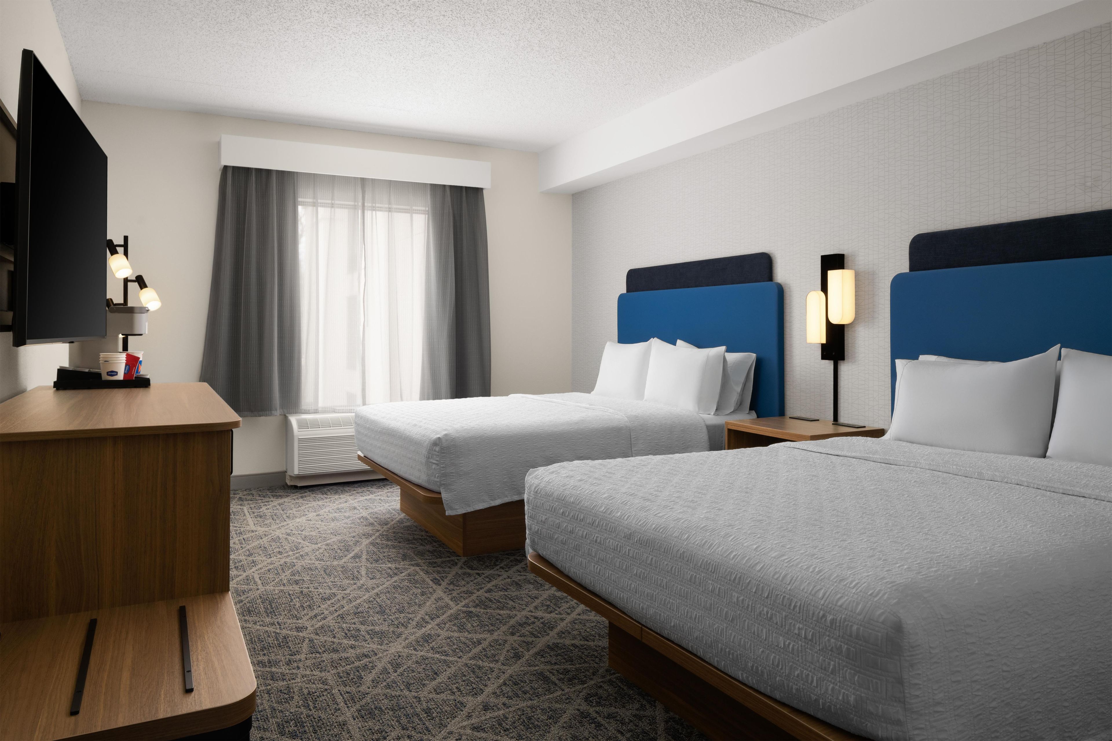 Een hotelkamer met twee bedden, een bureau, een televisie en een raam met gordijnen.