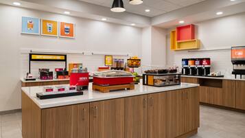 A breakfast bar with a coffee machine, a fruit basket, and a juice dispenser.