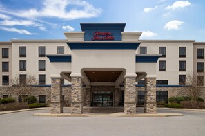 Entrada de un hotel con fachada de piedra, una decoración en blanco y azul, y un letrero que dice 'Hampton Inn & Suites'.