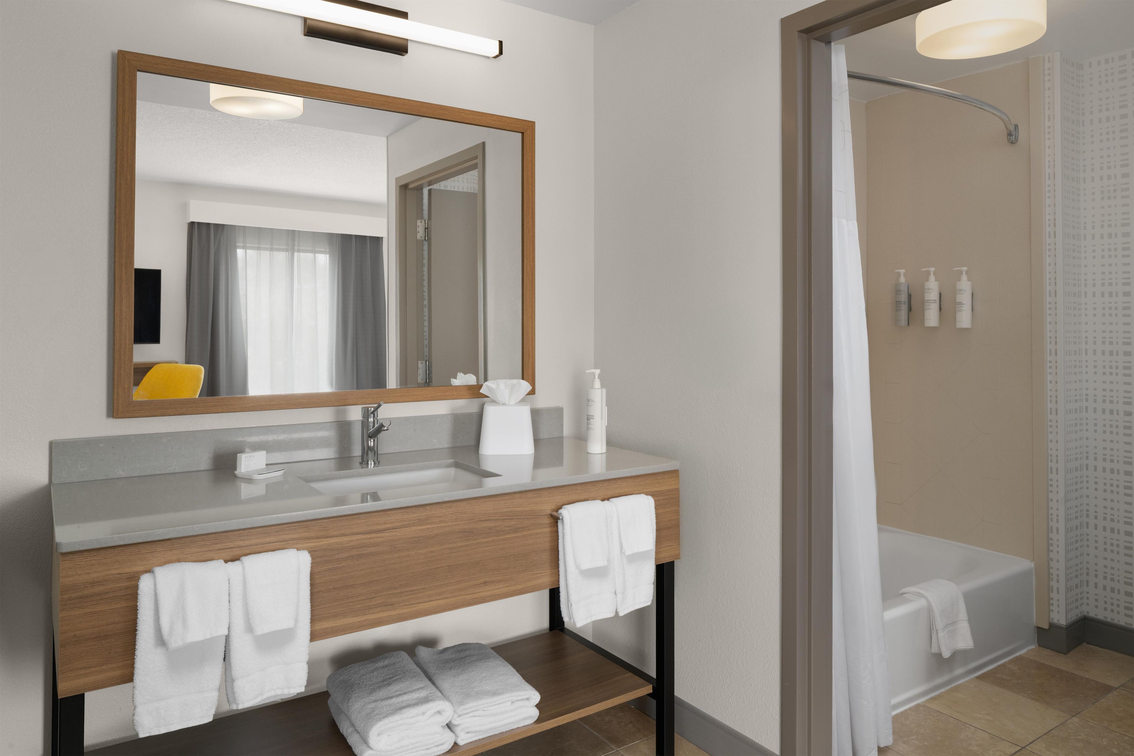 Un baño moderno con tocador de madera, un espejo grande, una bañera y una zona de ducha.