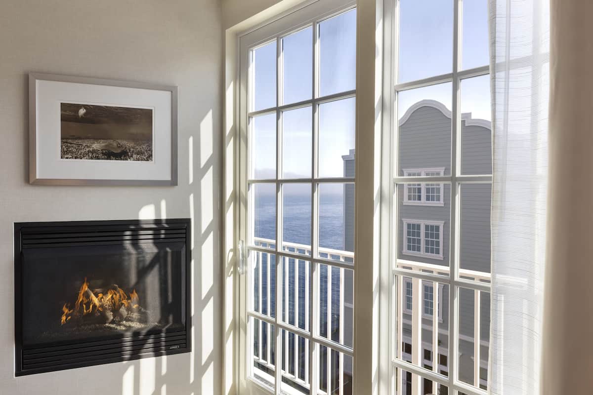 Quarto com lareira, um quadro na parede e uma janela ampla com vista para um edifício.