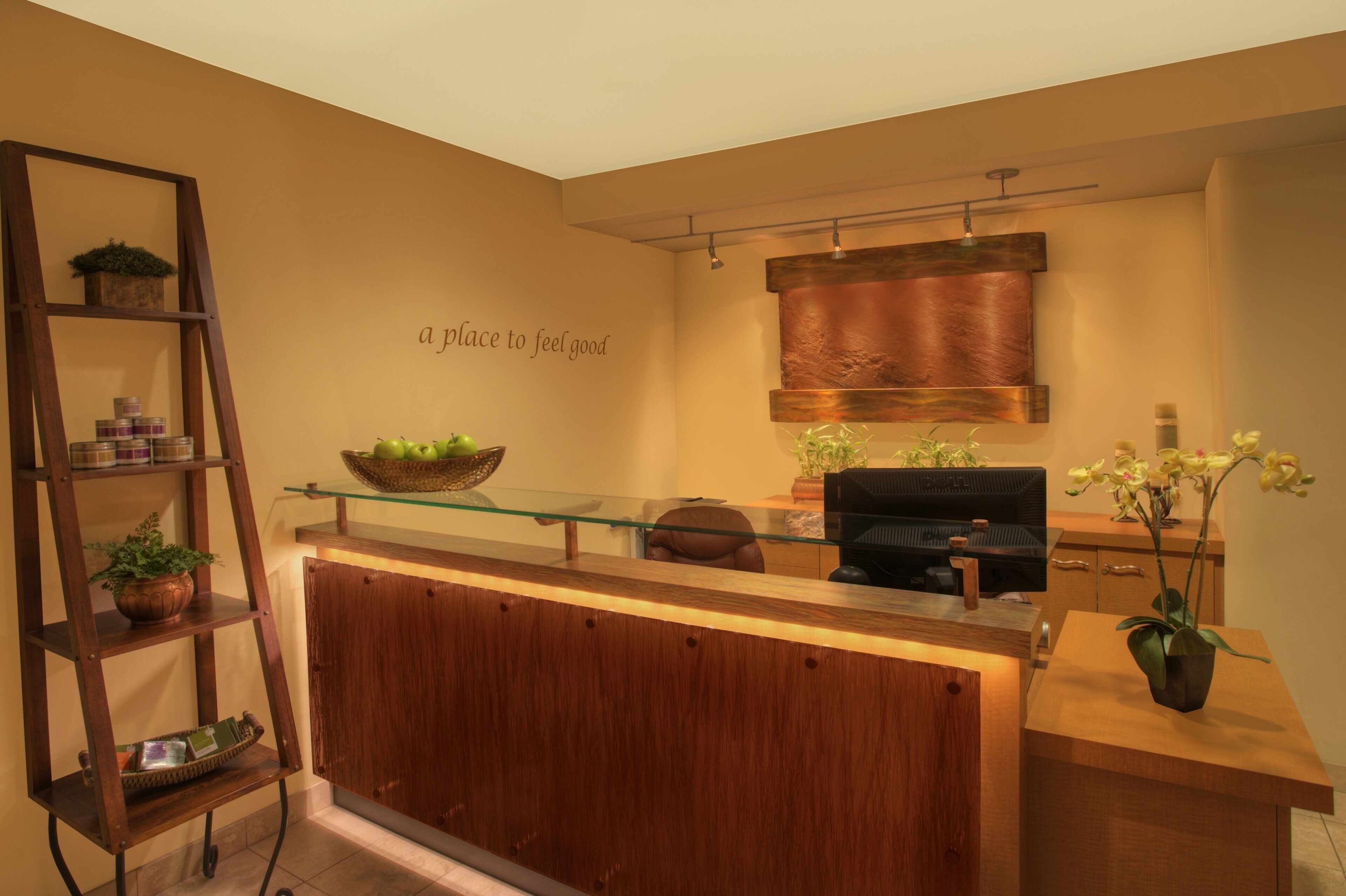 A reception area with a wooden counter, a glass display shelf, a black office chair, and a wall-mounted plant.