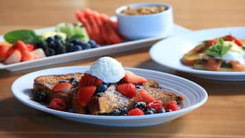 A breakfast setting with French toast topped with strawberries, blueberries, raspberries, and whipped cream, served on white plates.