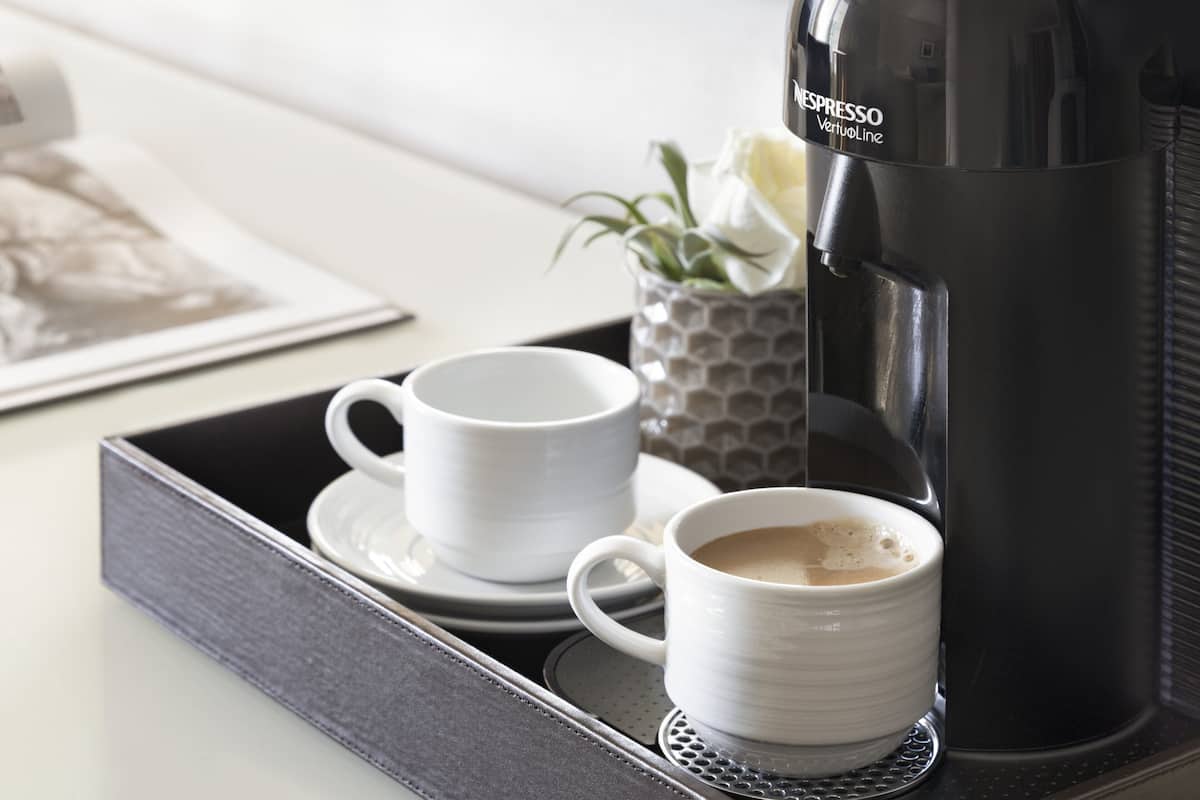Uma bandeja com duas xícaras brancas e uma cafeteira preta com a inscrição "ESPRESSO VerluoLine" sobre uma mesa.