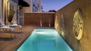 A swimming pool with a stone wall and a lounge area with chairs and a potted plant. - InterContinental the Clement Monterey by IHG (Monterey)