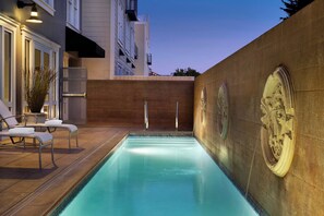Une piscine avec un mur en pierre et un espace détente comprenant des fauteuils et une plante en pot.