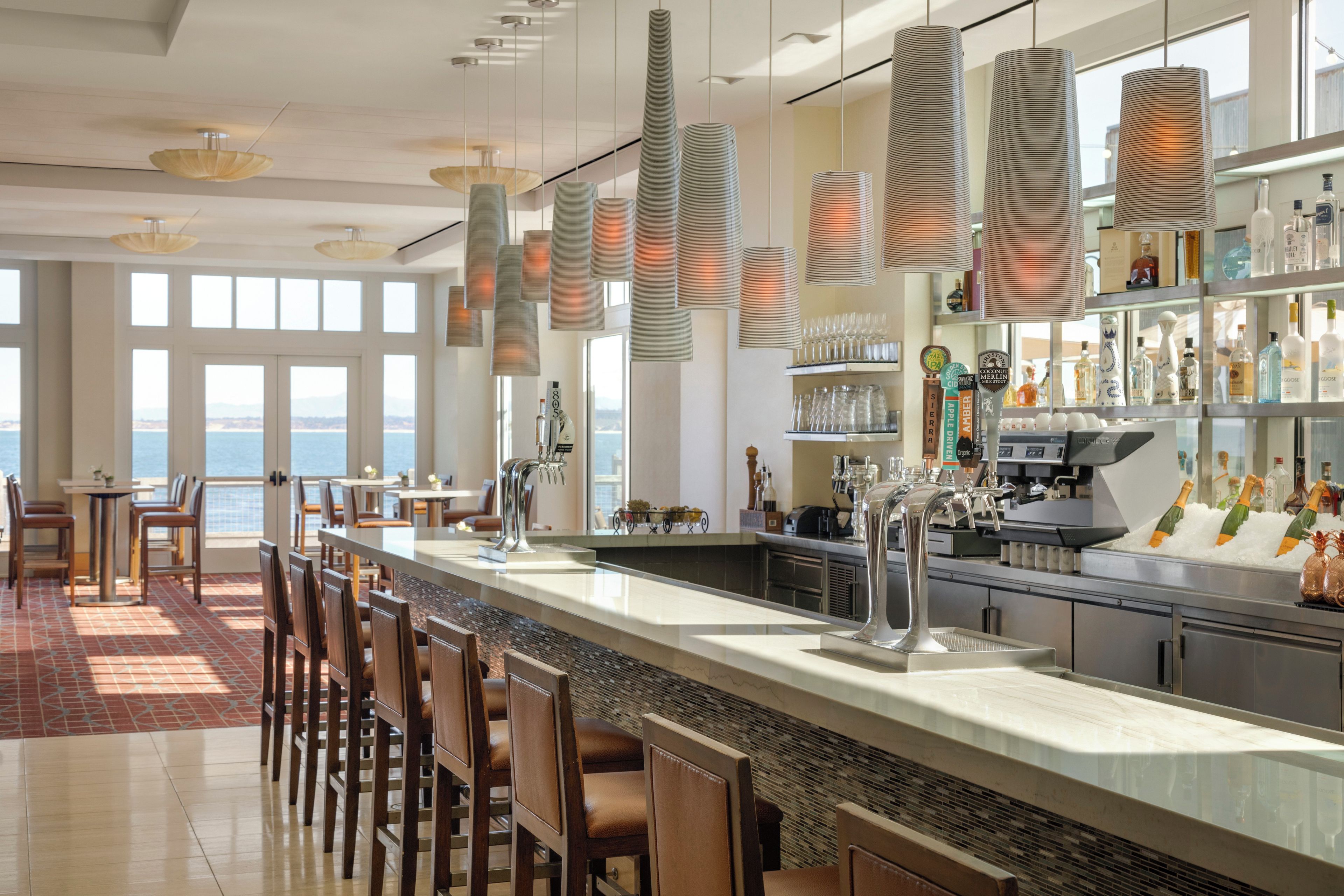 A bar area with a view of the sea, a bar counter, and a seating area with chairs.