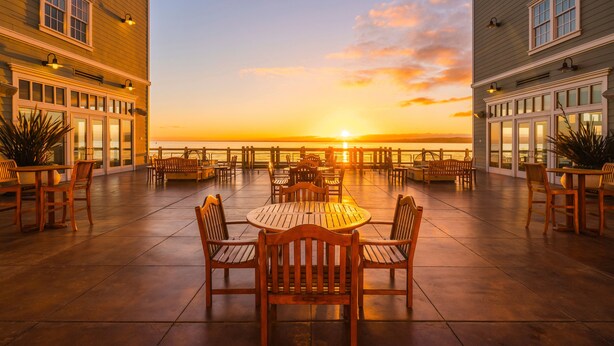A terrace with wooden tables and chairs, overlooking a sunset over the ocean. - InterContinental the Clement Monterey by IHG (Monterey)