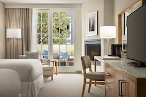 Habitación de hotel con cama, escritorio, silla, chimenea y una ventana grande con cortinas.