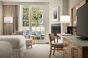 Habitación de hotel con cama, escritorio, silla, chimenea y una ventana grande con cortinas.