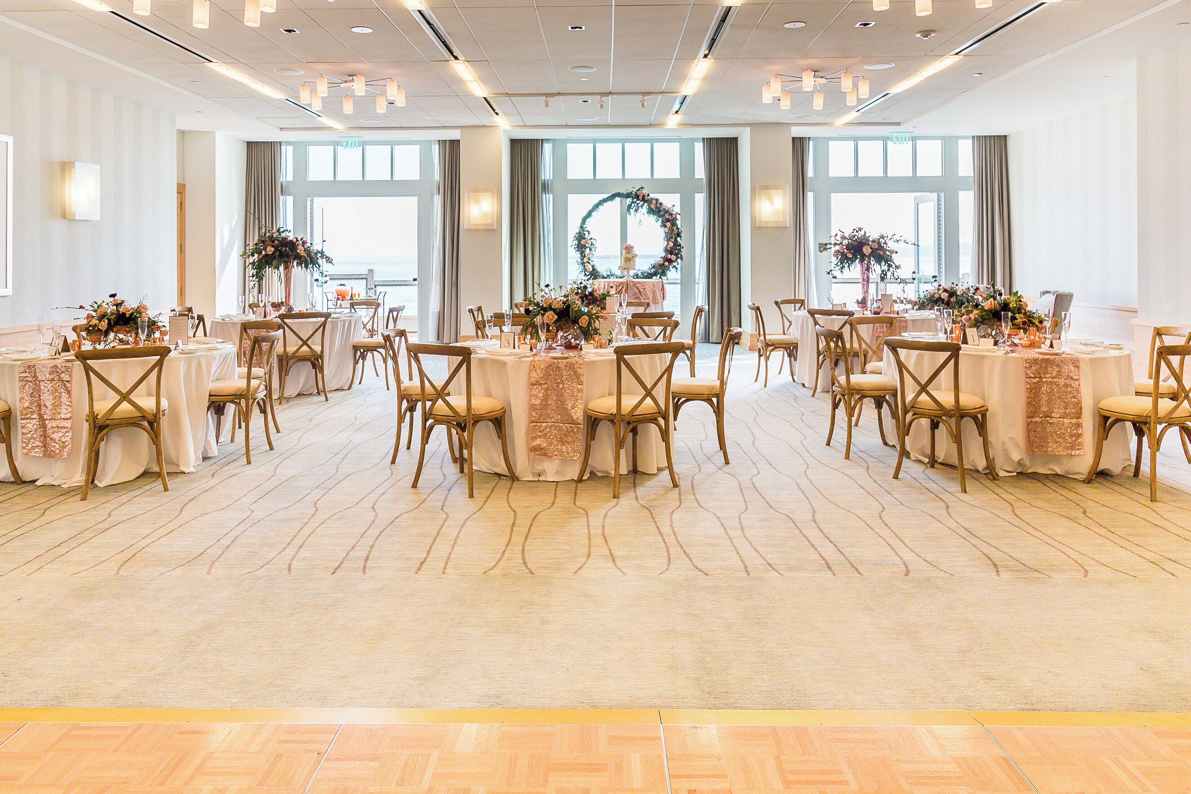 A banquet hall with round tables, chairs, and floral centerpieces.