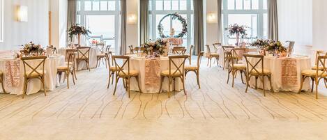 A banquet hall with round tables, chairs, and floral centerpieces.