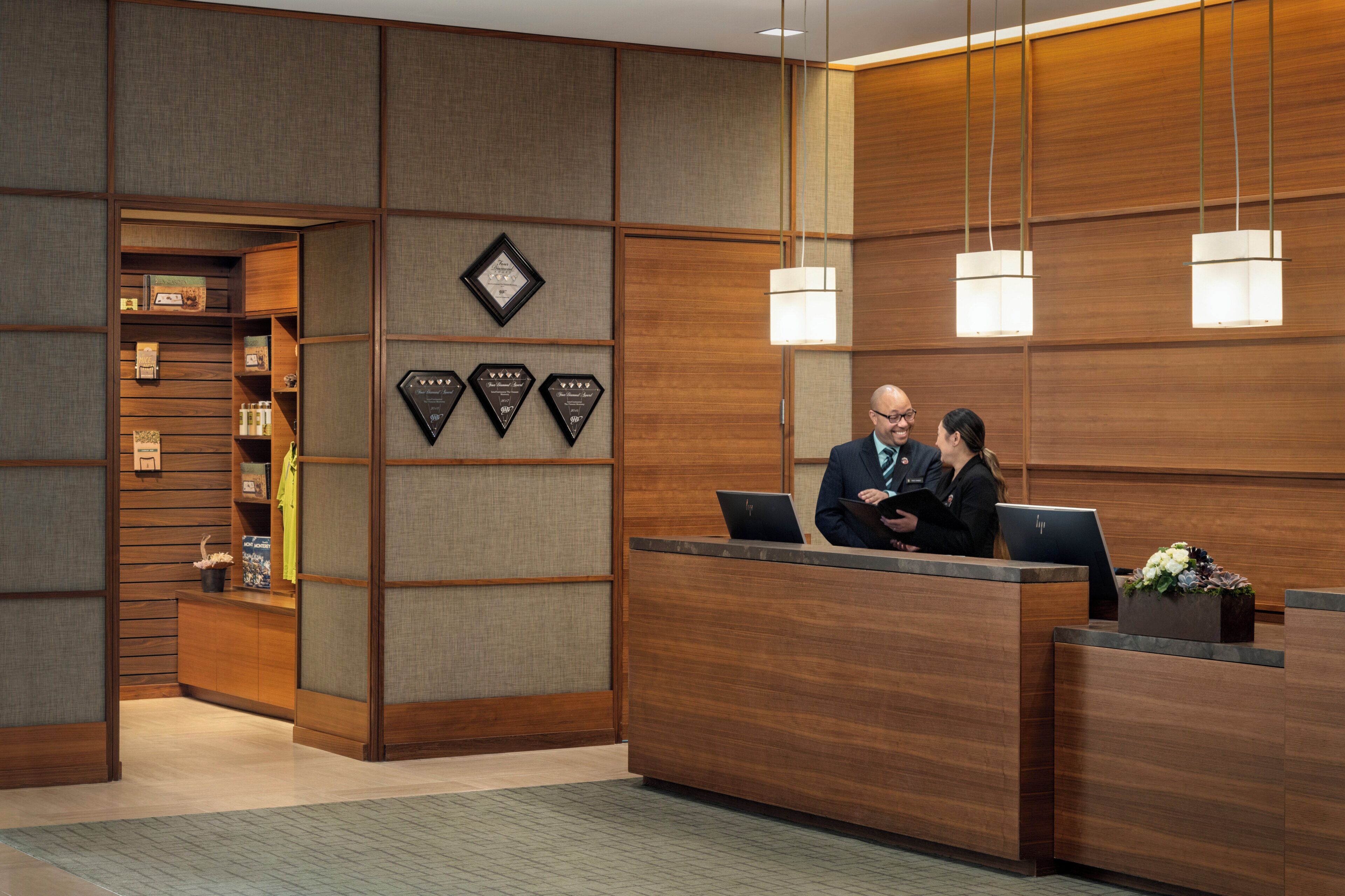 A reception desk with a wooden finish, a bulletin board with awards, and a modern pendant light fixture.