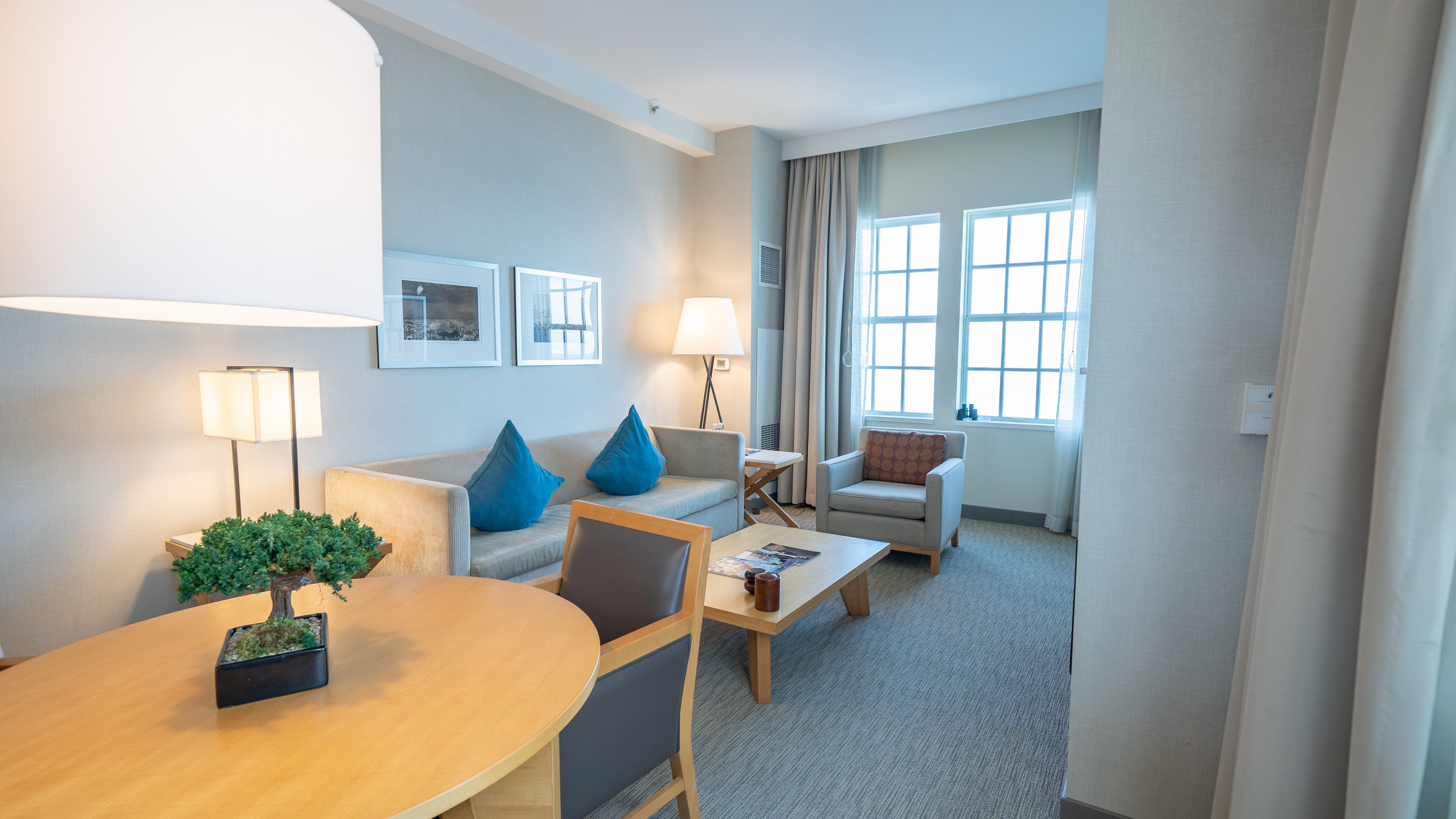 Een moderne hotelkamer met een ronde eettafel, twee banken, een klein bijzettafeltje en een raam met gordijnen.