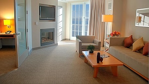 A hotel room with a sofa, a coffee table, a TV, a fireplace, and a large window with curtains. - InterContinental the Clement Monterey by IHG (Monterey)