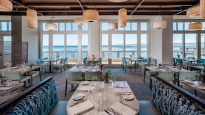 A restaurant with tables set for dining, large windows with a view of the sea, and hanging pendant lights. - InterContinental the Clement Monterey by IHG (Monterey)