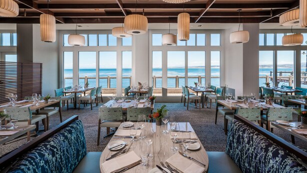 A restaurant with tables set for dining, large windows with a view of the sea, and hanging pendant lights. - InterContinental the Clement Monterey by IHG (Monterey)