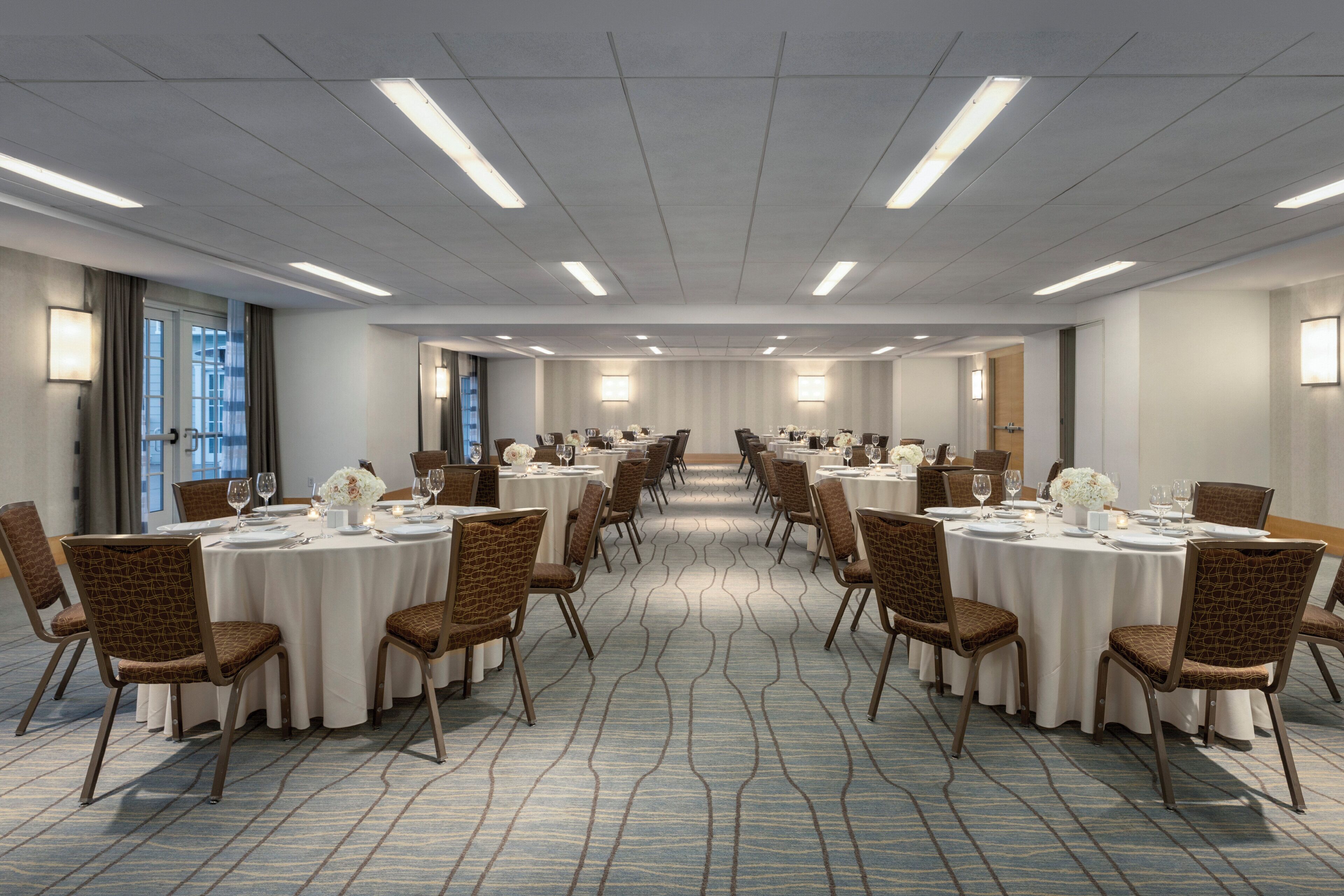 Sala de conferências com mesas redondas, cadeiras e iluminação pendente.