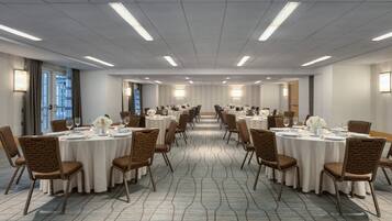 Sala de conferências com mesas redondas, cadeiras e iluminação pendente.
