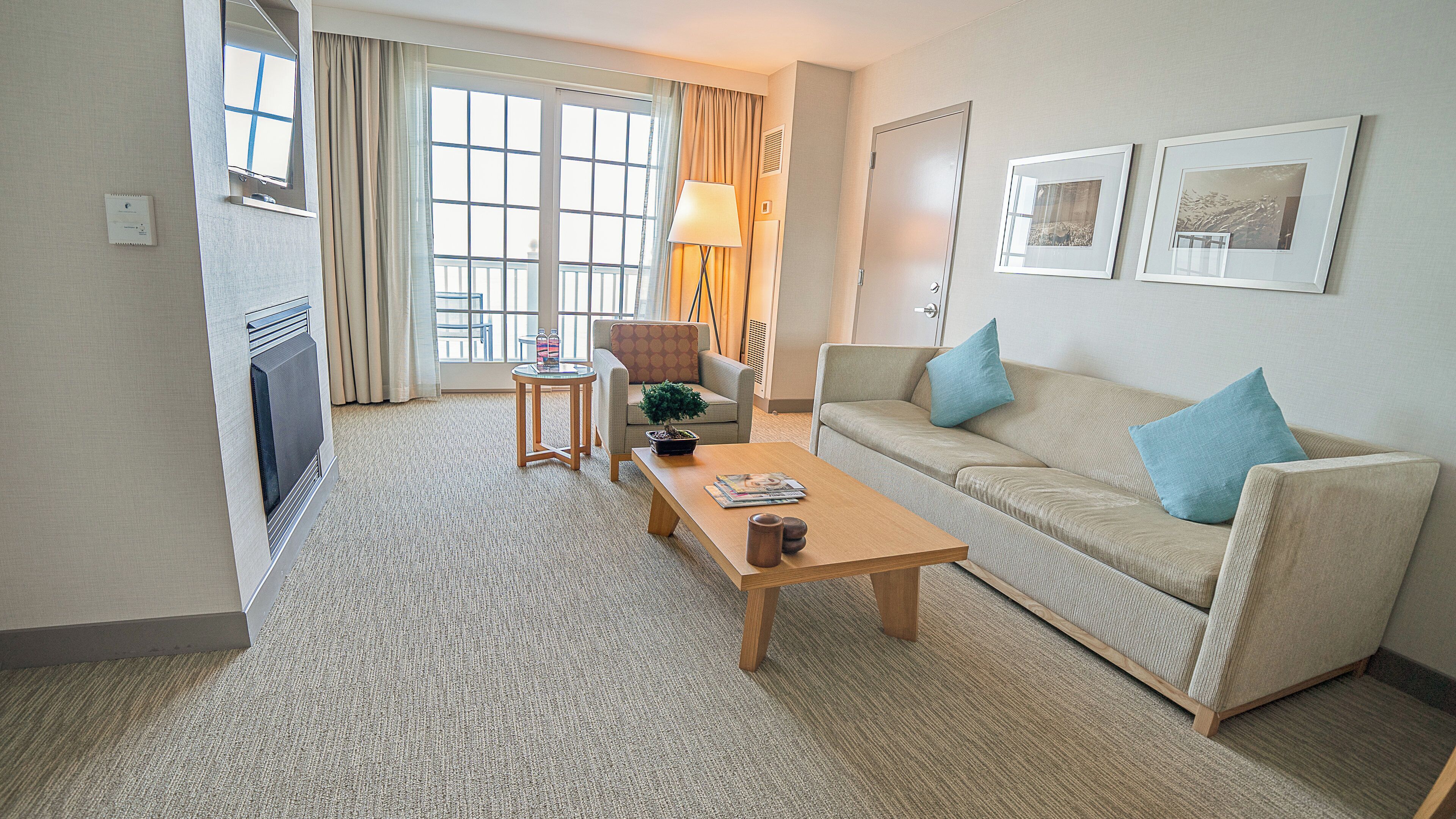A hotel room with a sofa, a coffee table, a chair, a lamp, and a window with curtains.