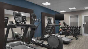 Gimnasio con cintas de correr, elípticas y un televisor montado en la pared.