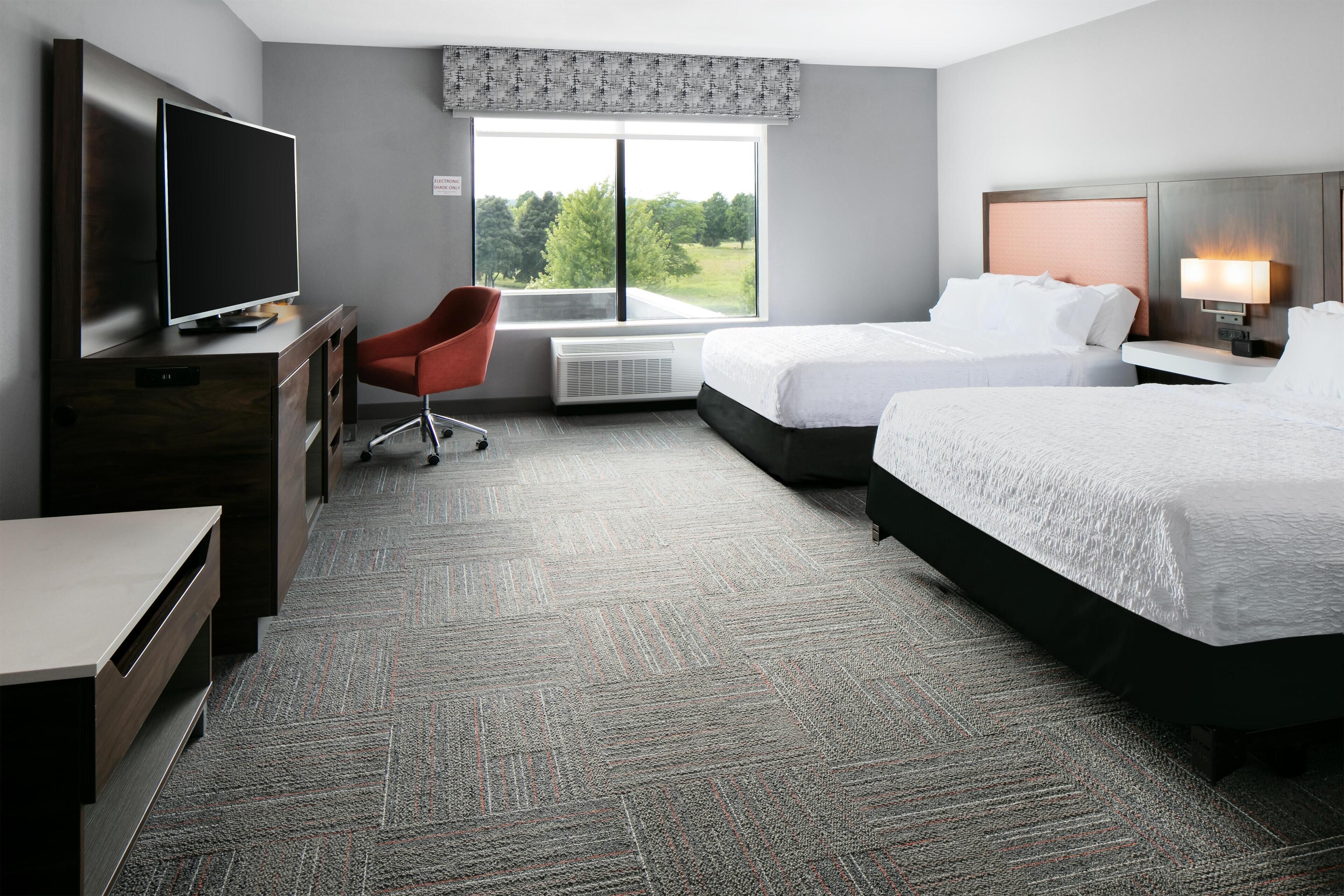 A hotel room with two beds, a TV, a desk, a chair, and a window with a view.