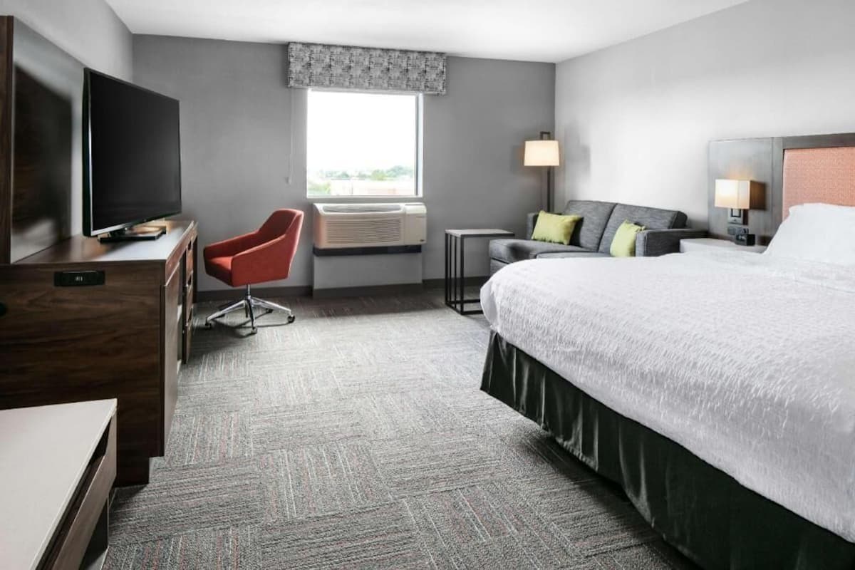 A hotel room with a bed, a TV, a desk, a chair, a window, and a lamp.