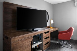 Una habitación moderna con un televisor de pantalla plana sobre un mueble de madera, una silla de escritorio roja y una lámpara de escritorio.
