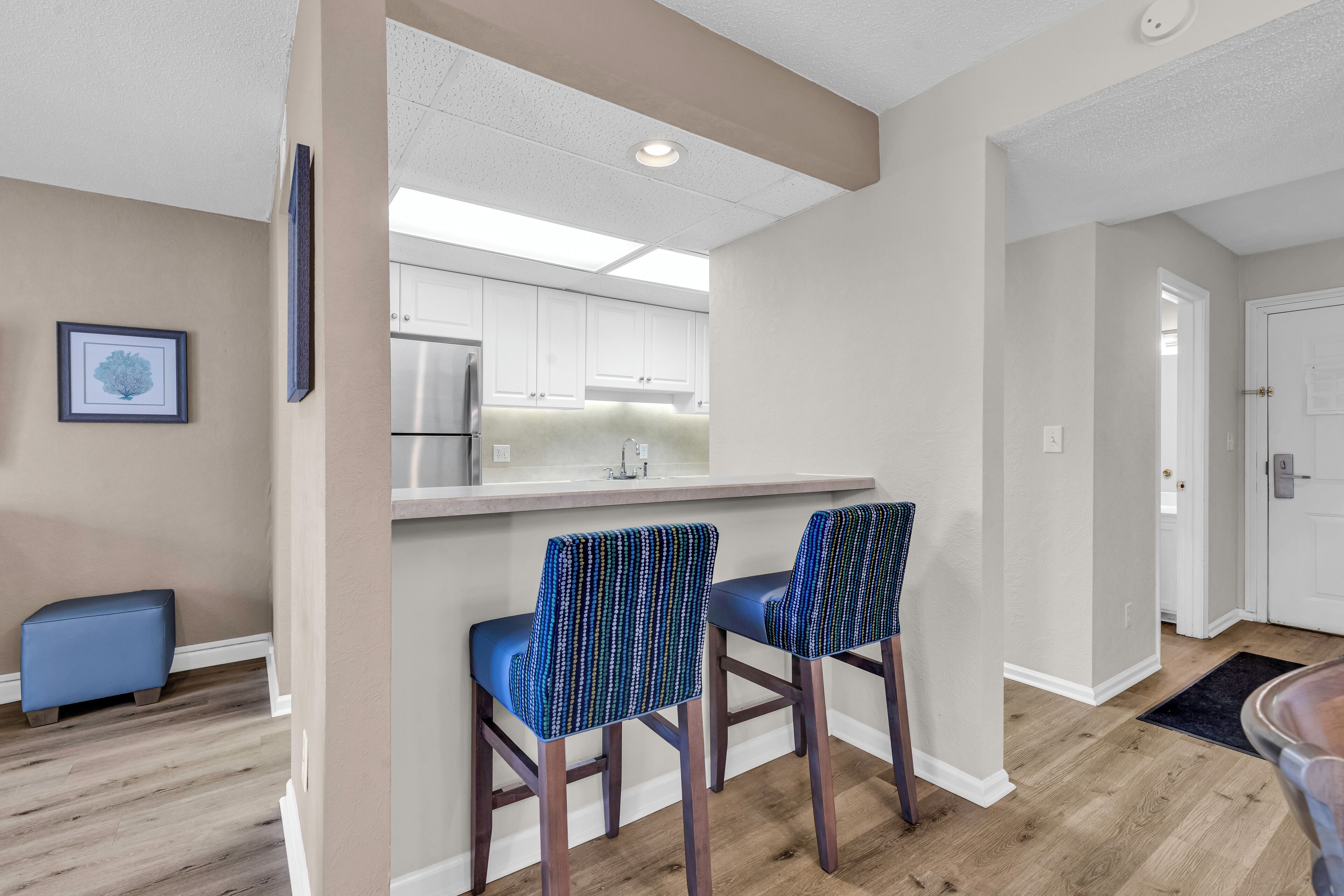 A modern kitchen with white cabinets, a stainless steel refrigerator, and two bar stools with patterned upholstery.