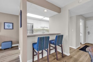 A modern kitchen with white cabinets, a stainless steel refrigerator, and two bar stools with patterned upholstery.