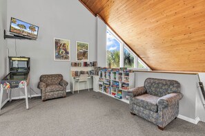 A cozy reading nook with a wooden ceiling, a television, a bookshelf, two patterned armchairs, and a desk.