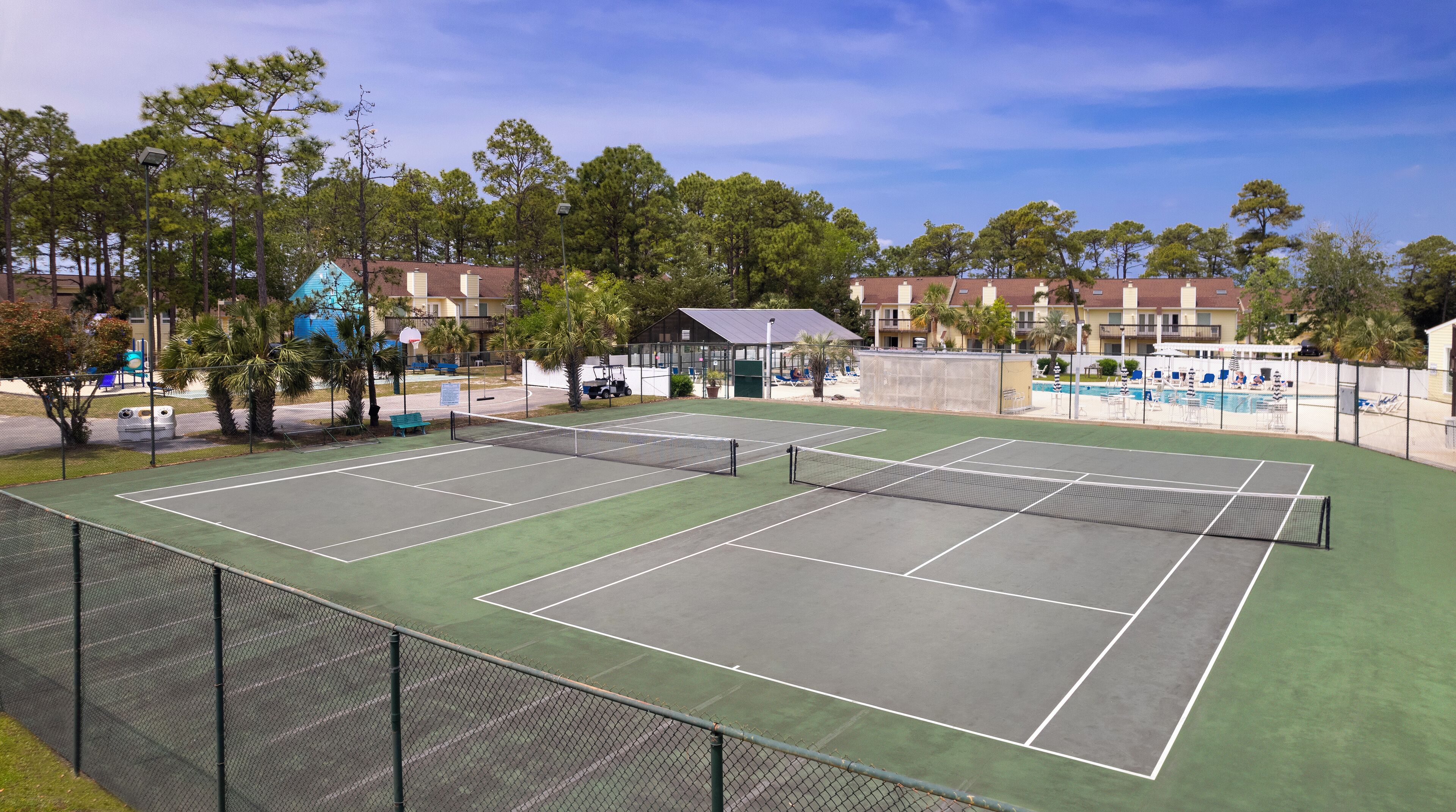 Canchas de tenis múltiples, rodeadas por una valla, y una piscina al fondo.