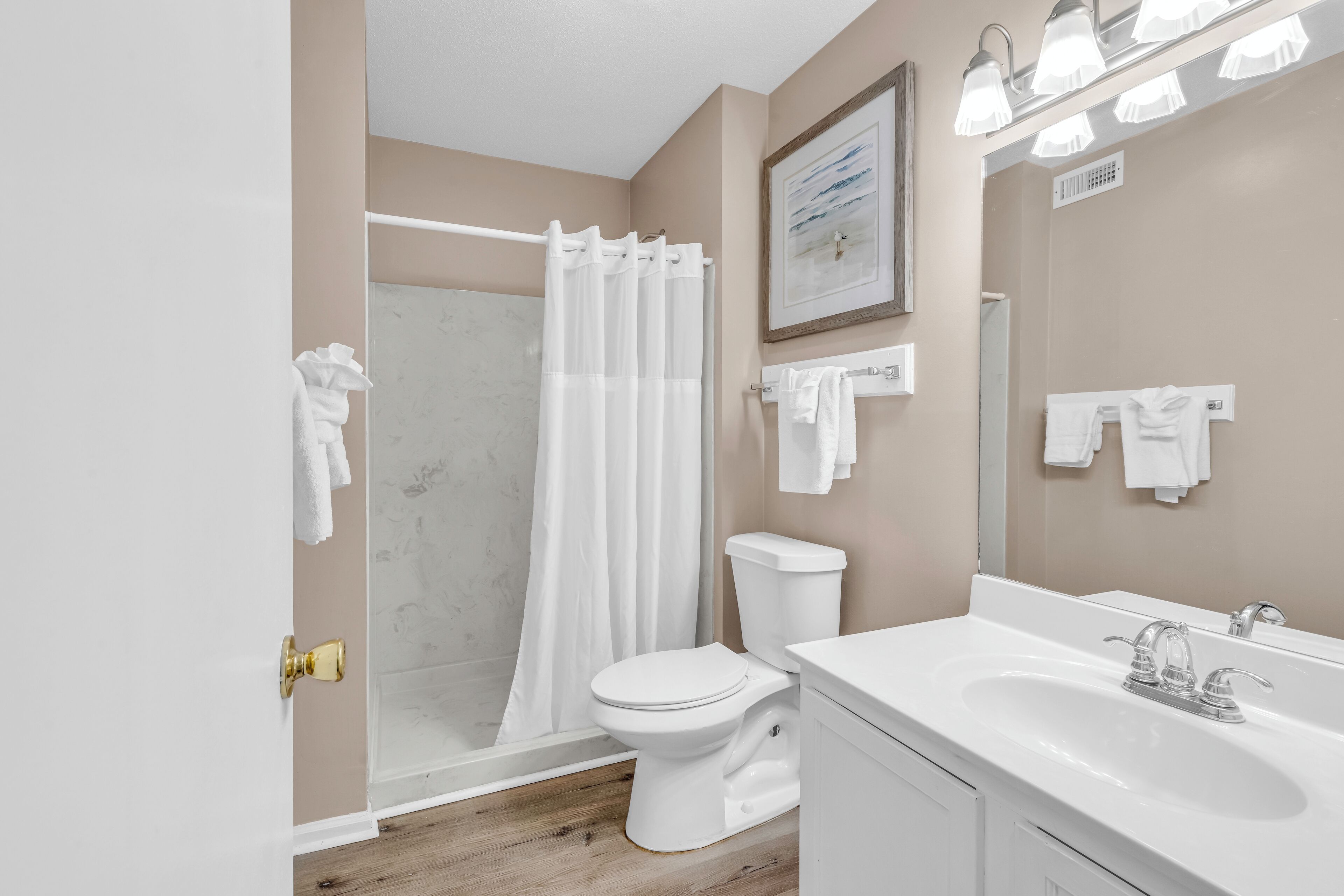 A bathroom with a toilet, sink, shower, and a framed picture on the wall.