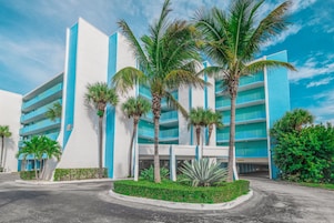 Un hotel moderno con fachada azul y blanca, varios pisos y palmeras en primer plano.