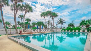 A rectangular swimming pool with a tiled edge, surrounded by palm trees and lounge chairs. - Turtle Reef Club (Jensen Beach)