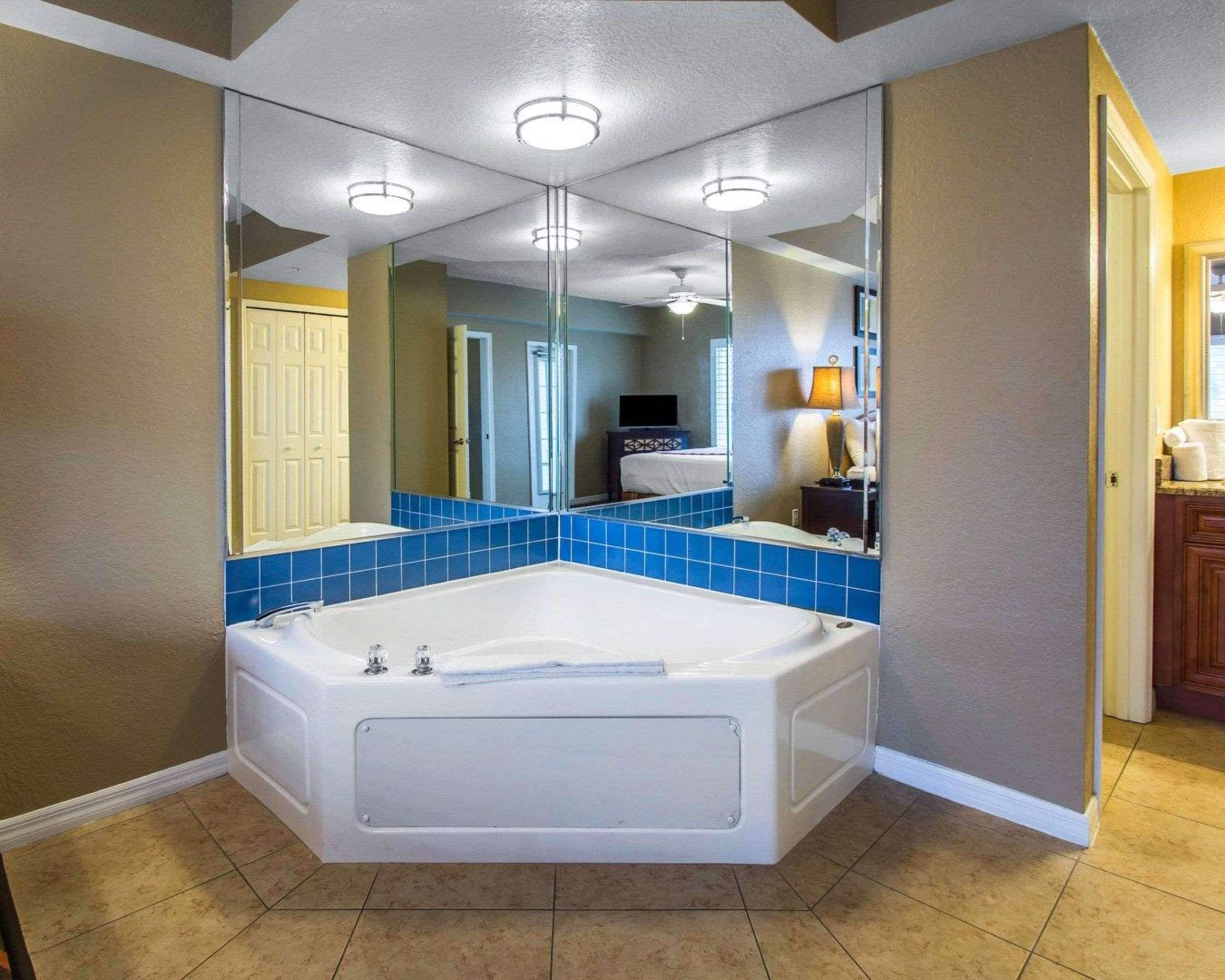 Une salle de bain avec une baignoire d’angle, des carreaux bleus, un grand miroir et un ventilateur de plafond.