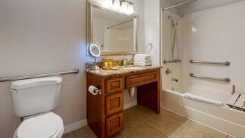 A bathroom with a toilet, vanity with a mirror, and a bathtub with grab bars.