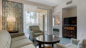 A hotel room with a sofa, armchair, a small round table, a TV on a wooden cabinet, and a patterned curtain. - Bluegreen Vacations Orlando's Sunshine, Ascend Collection Resort (Orlando)
