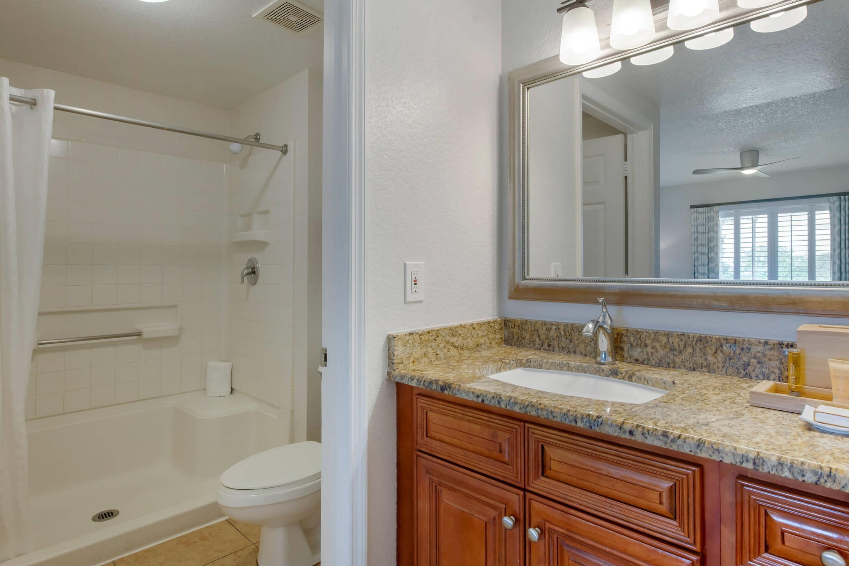 Un baño con ducha, inodoro, tocador con lavabo y espejo.