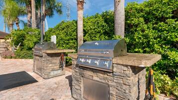 Un espace barbecue extérieur doté de foyers en pierre, entouré d’une végétation luxuriante et de palmiers.