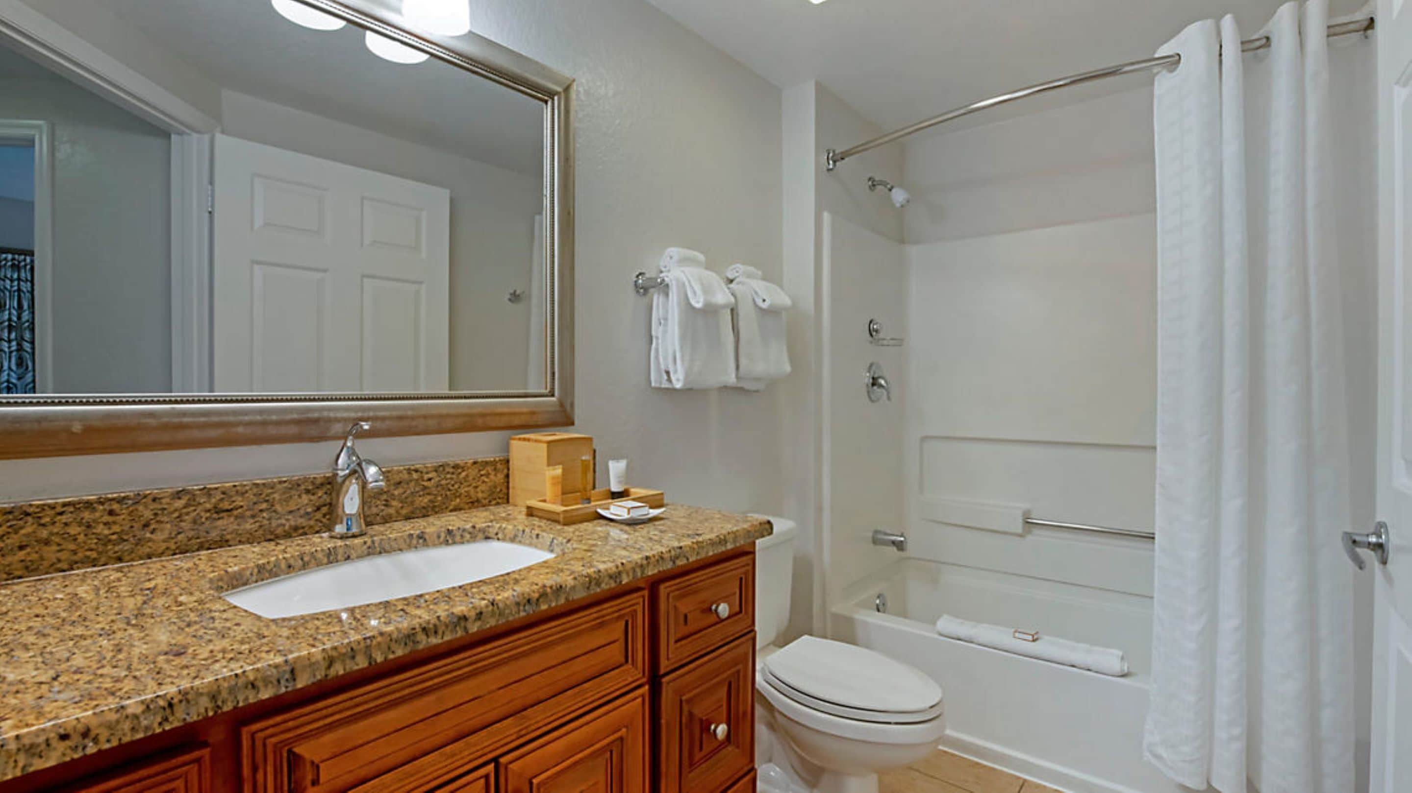 A bathroom with a granite countertop sink, wooden vanity, a toilet, a bathtub, and a shower with a glass door.