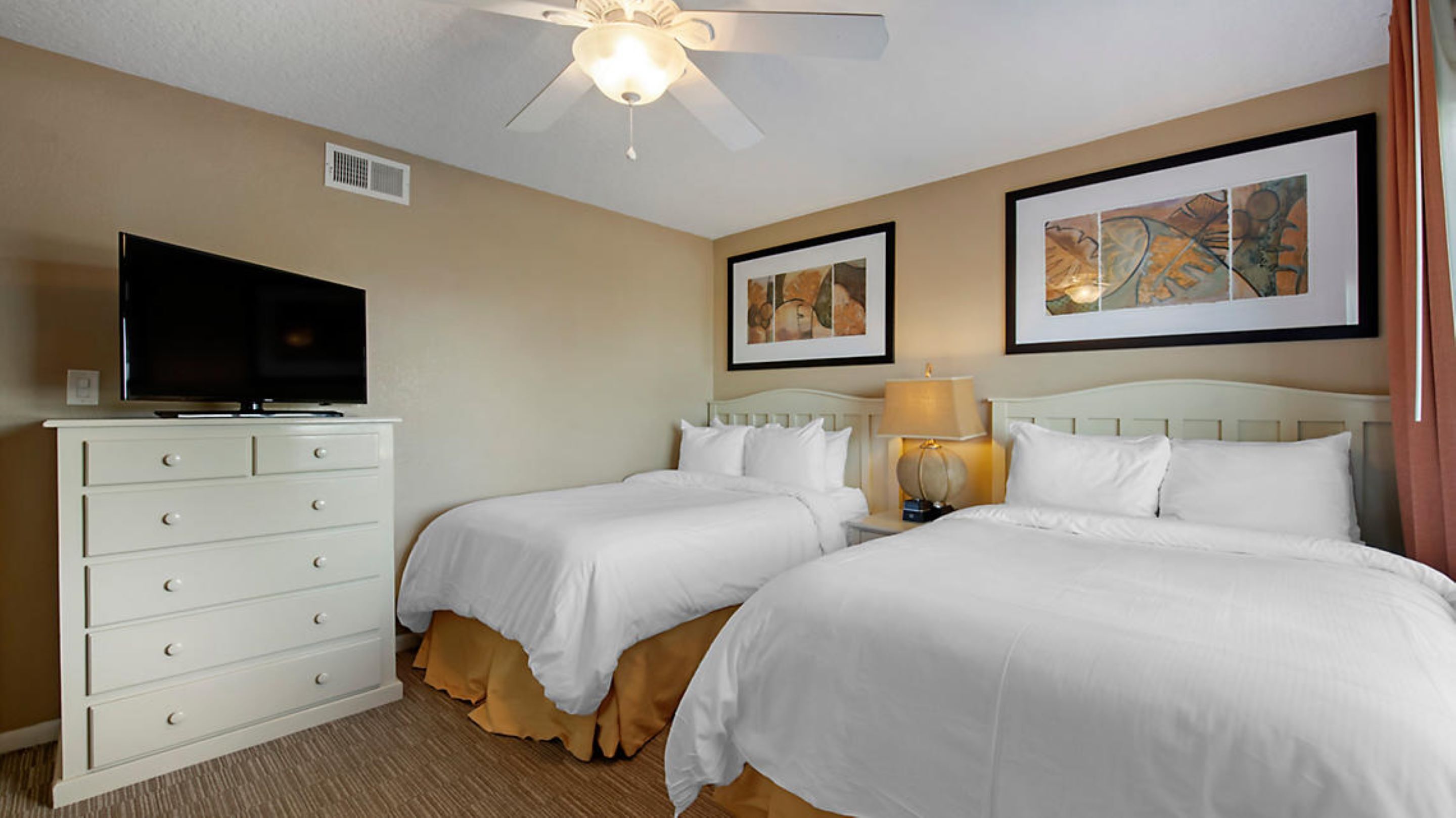 A hotel room with two beds, a TV on a dresser, and artwork on the walls.