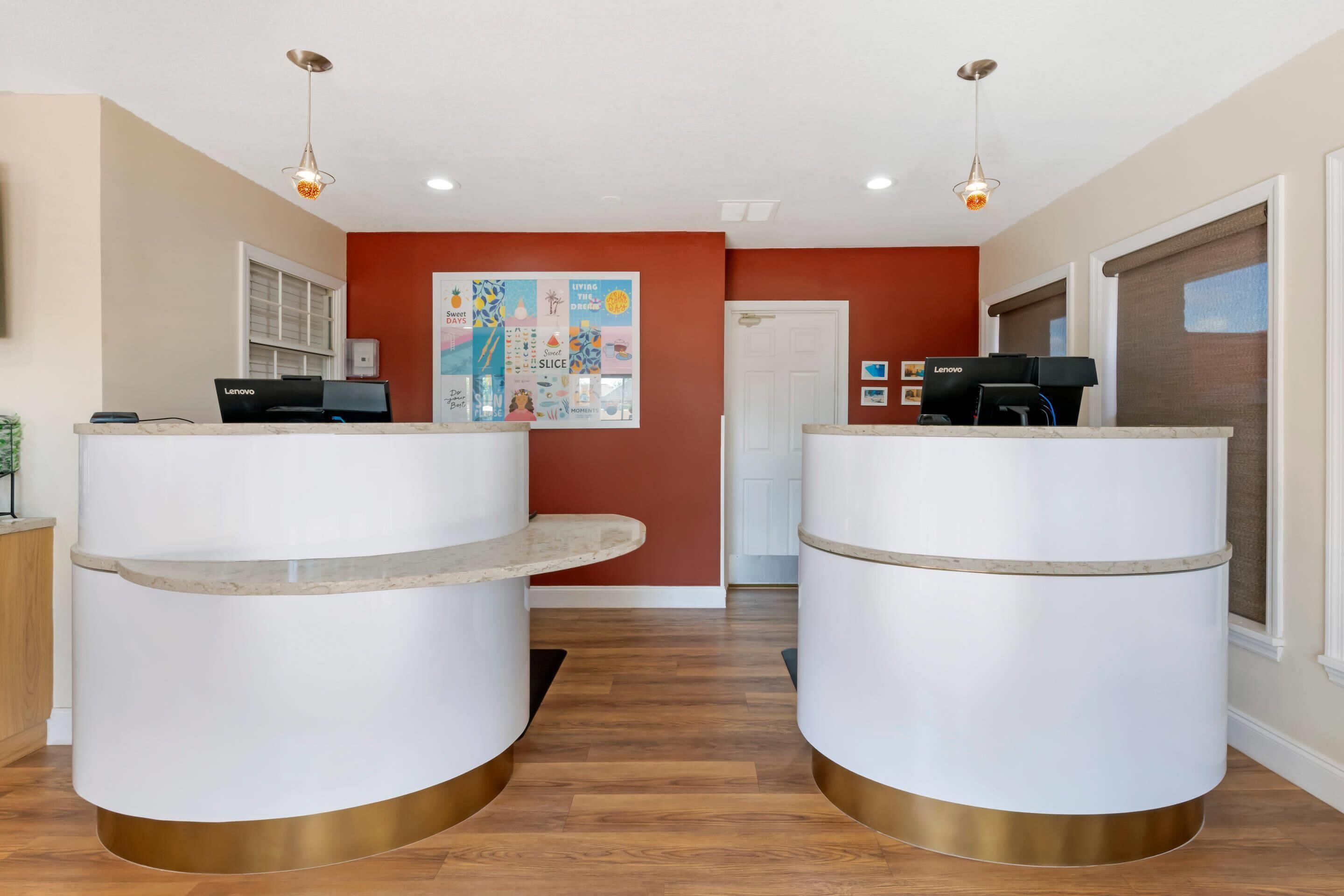A reception area with two white reception desks, a red accent wall, and a poster on the wall.