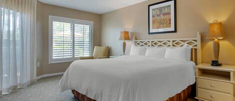 A hotel room with a large bed, a nightstand with a lamp, a window with blinds, and a ceiling fan.