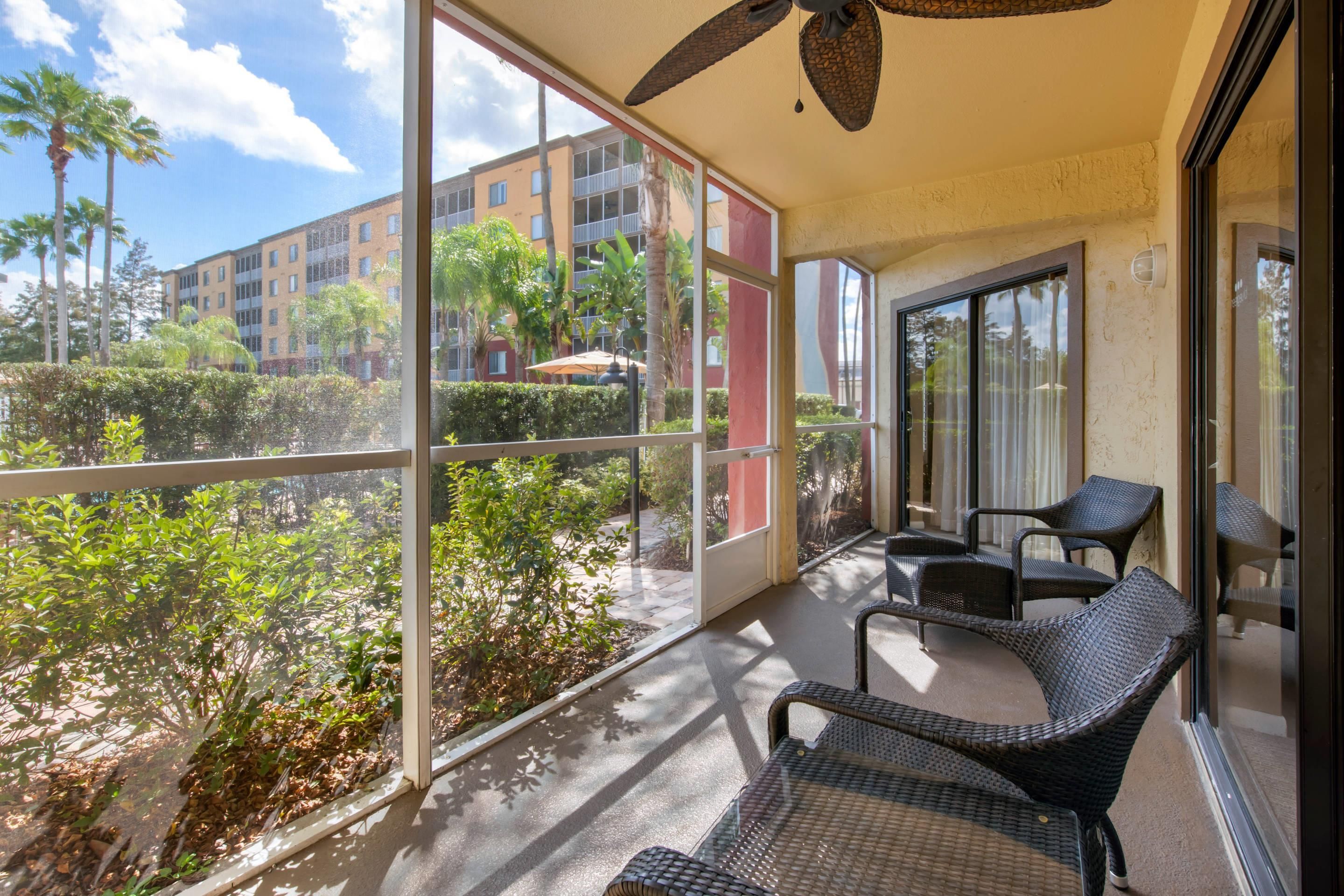 Un balcon avec des fauteuils en osier, un ventilateur de plafond et une vue sur un immeuble et la verdure.