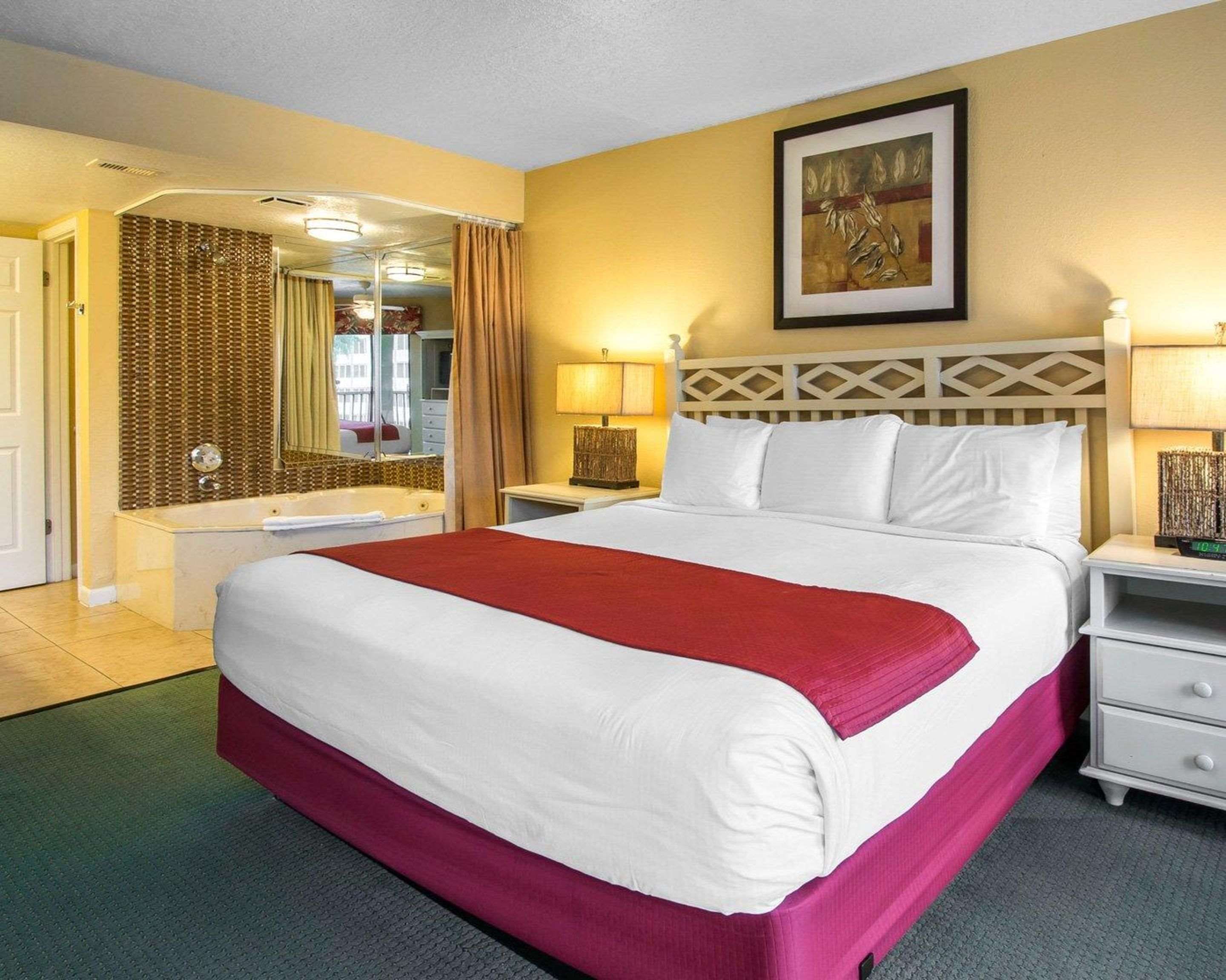 Une chambre d’hôtel avec un grand lit, une salle de bain avec une baignoire, un miroir et un tableau au mur.