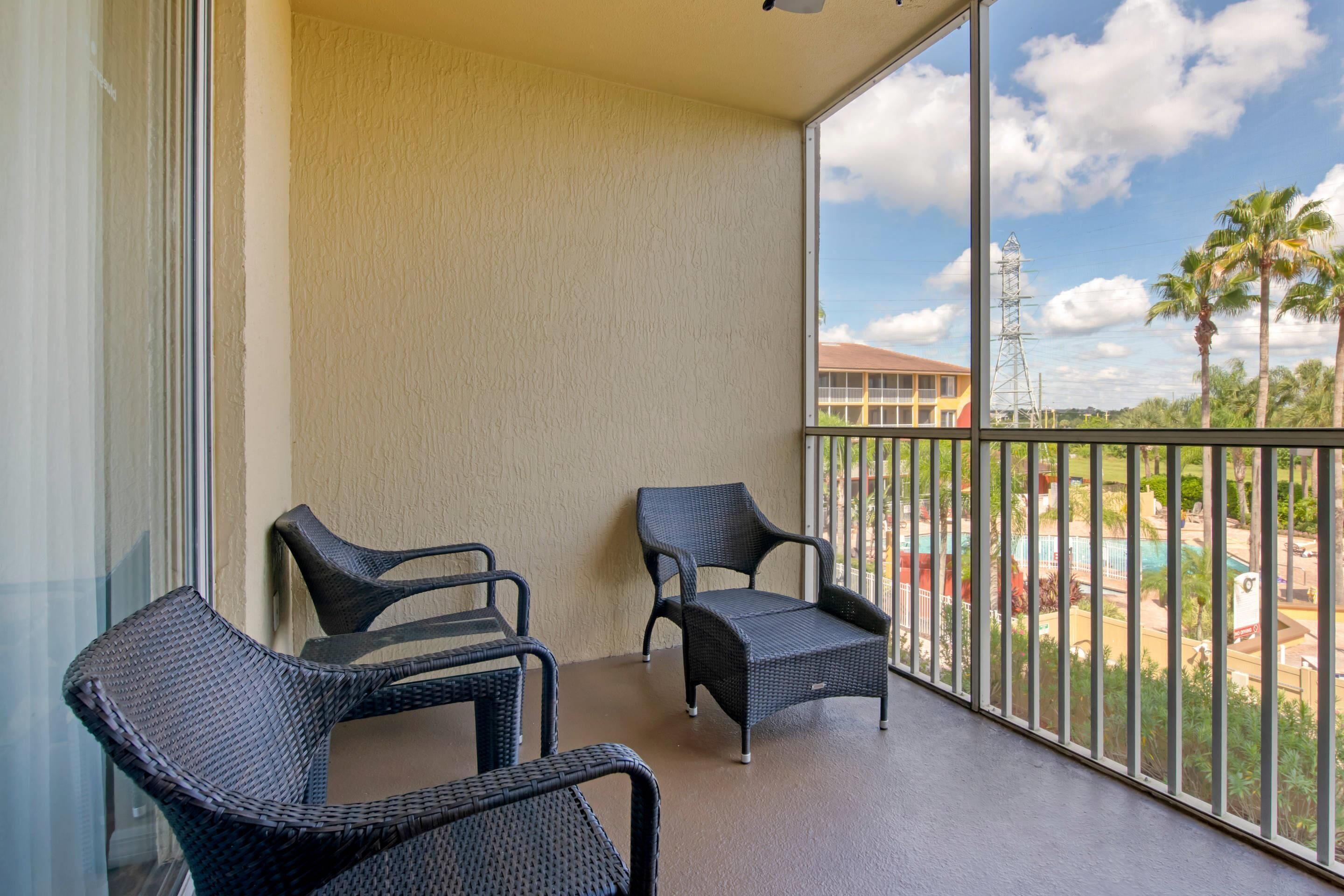 A balcony with two wicker chairs and a view of a pool and palm trees.